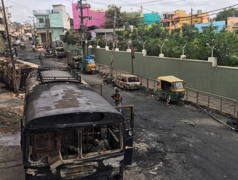 `Television news camera operator films burnt police bus and other private vehicles after violence erupted between police and protesters over a reported derogatory Facebook post about Islam's Prophet Mohammad in Bengaluru